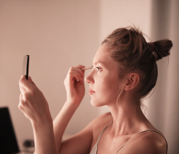 Women putting on eye makeup in mirror